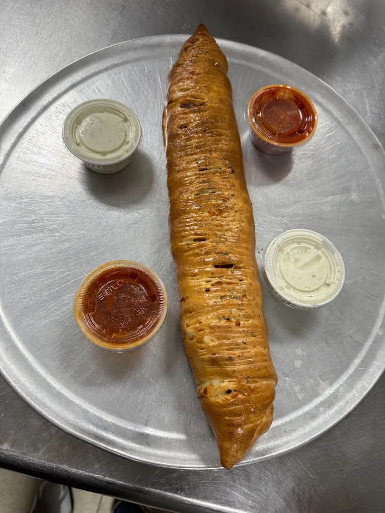 A long golden stromboli with four cups of dipping sauce